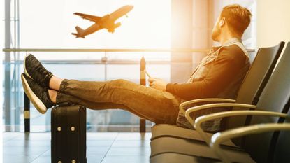 Man resting in an airport while watching a plane take off