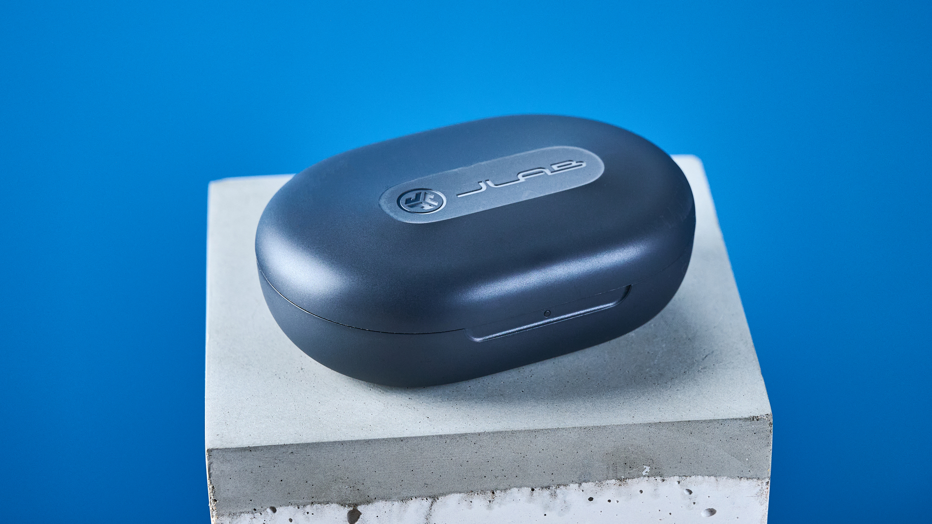 the jlab go sport+ earbuds photographed against the blue tom's guide background, showing charging case and wearing style