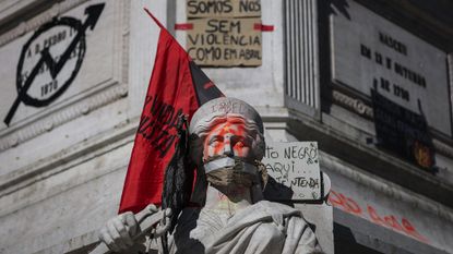 Spray paint, flags and protest signs plaster the Column of Pedro IV during a protest against housing shortages, soaring rents and low wages at Rossio Square in Lisbon, Portugal