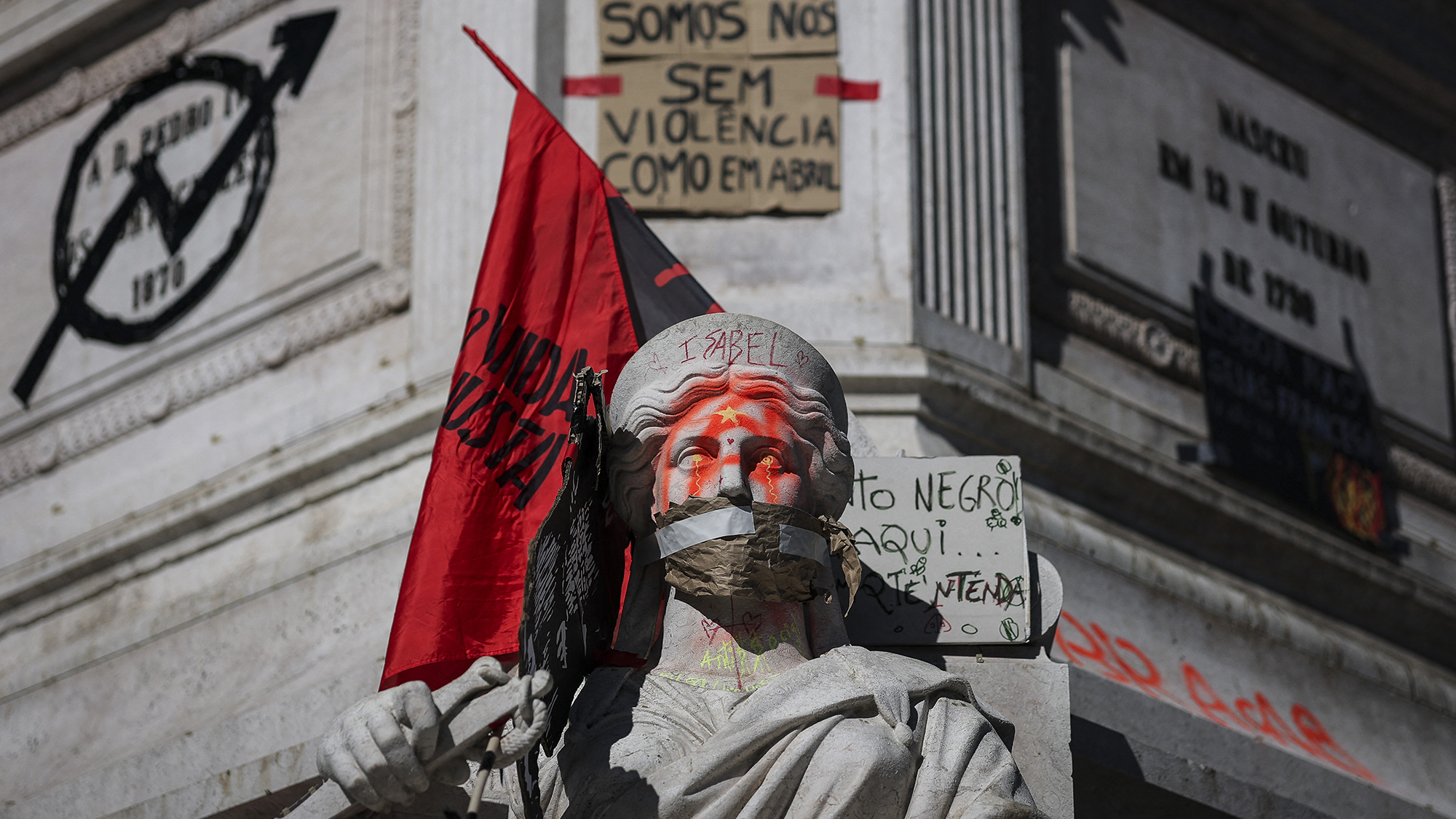 Spray paint, flags and protest signs plaster the Column of Pedro IV during a protest against housing shortages, soaring rents and low wages at Rossio Square in Lisbon, Portugal