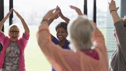 Group of smiling women standing in a circle with their arms raised overhead