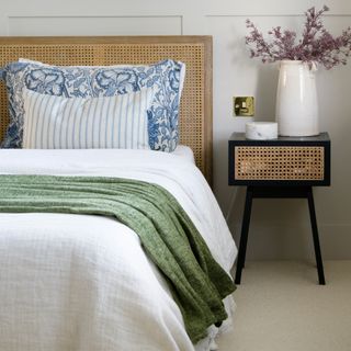 A bedroom featuring a rattan headboard, rattan side table and green, white and blue bedding