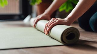 Woman's hands rolling up yoga mat on wooden floor