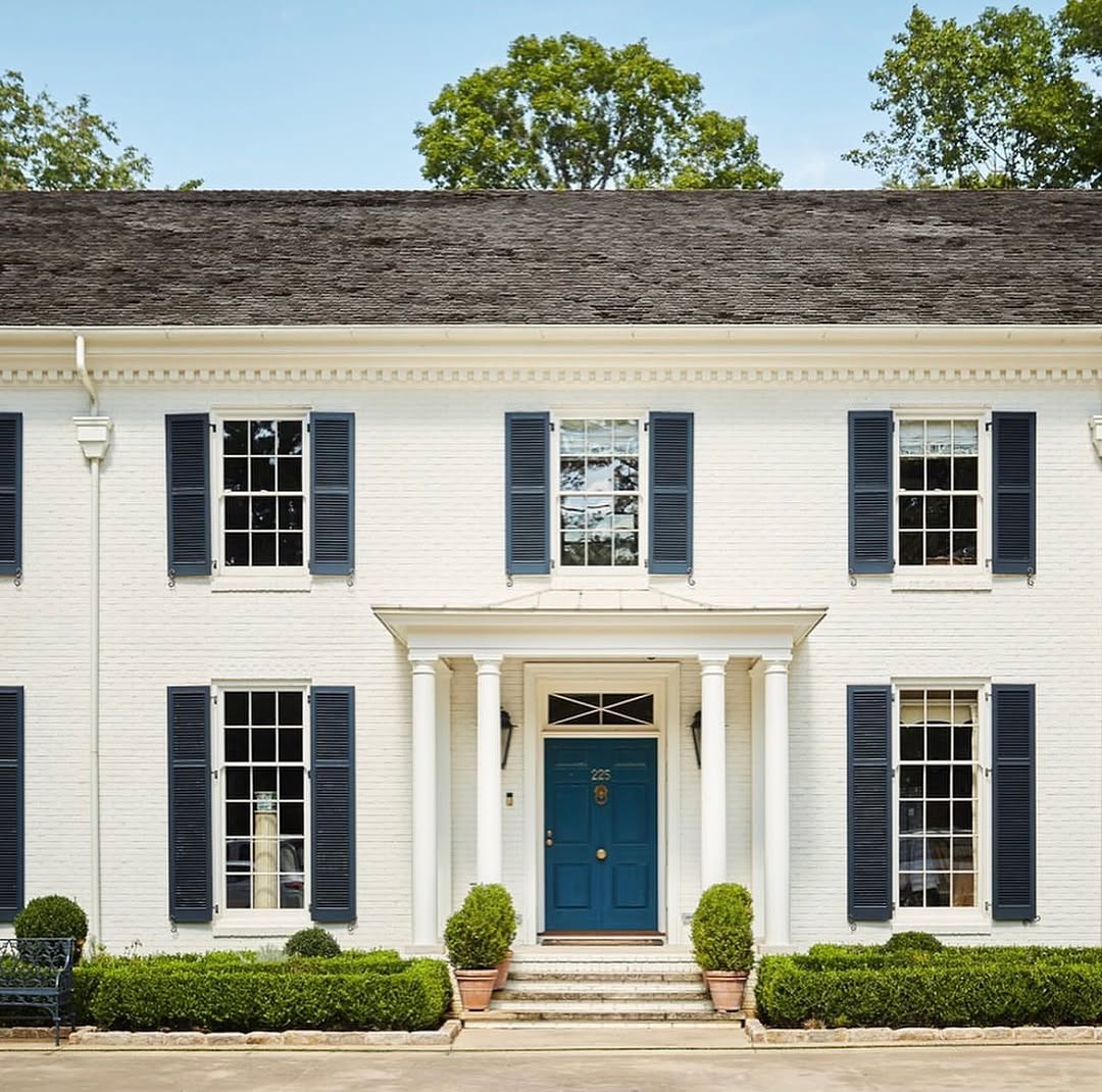 classic white colonial with navy front door and shutters. boxwoods in front