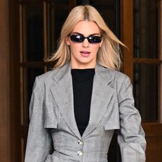 Kendall wears black sunglasses, a black shirt, and a gray cinched waist blazer.