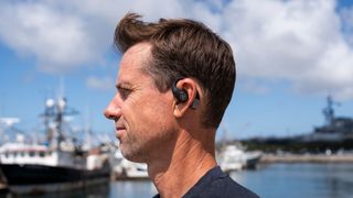 A man wearing JLab Epic Open Sport earbuds with a harbour in the background