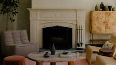 Living room with cream walls, purple, pink and rust rug, lilac armchair, green and rust stools, rattan chairs and burl wood sideboard