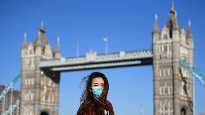 A woman wears a mask by London's Tower Bridge.