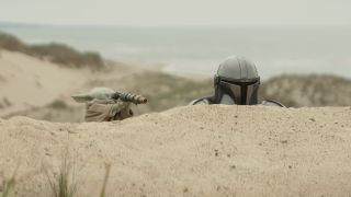 The Mandalorian peering over sand dune, Grogu doing the same with a small telescope