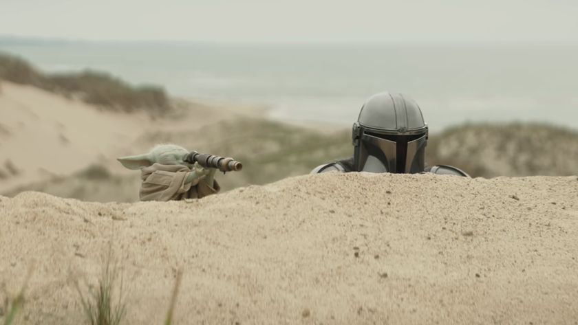 The Mandalorian peering over sand dune, Grogu doing the same with a small telescope