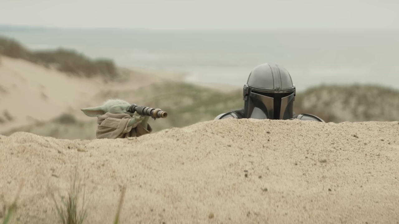 The Mandalorian peering over sand dune, Grogu doing the same with a small telescope