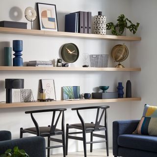 white wall with wooden shelf with show pieces clock and chairs