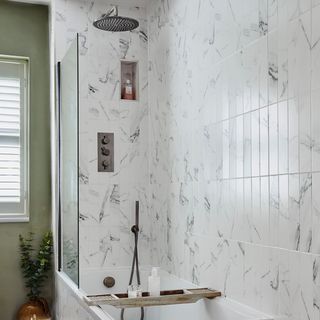 A bathtub with a shower head tiled in a marble effect
