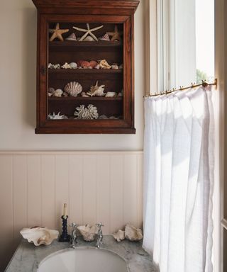 vintage bathroom with a linen sheer cafe curtain and a cabinet filled with shells