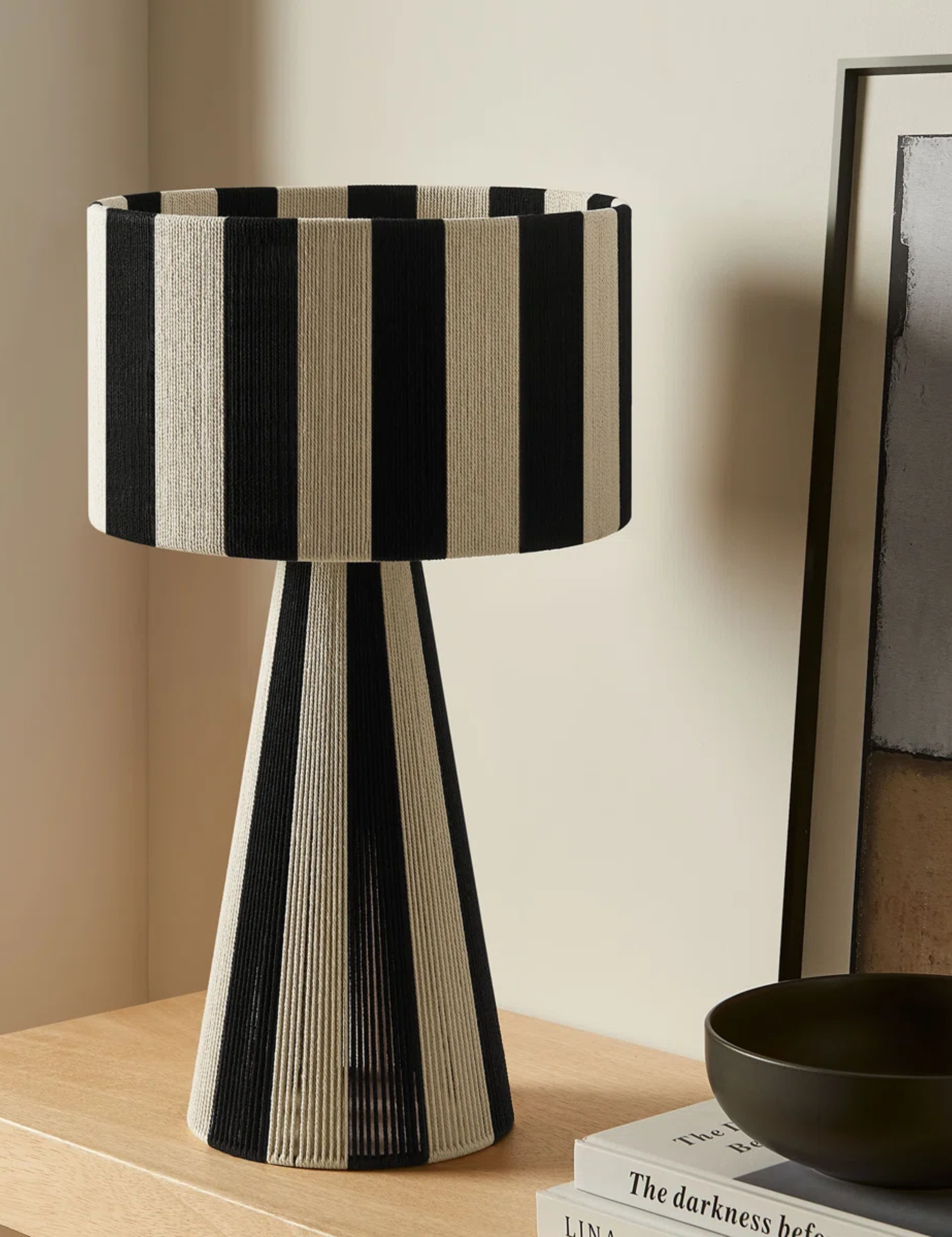 Striped table lamp pictured alongside a stack of coffee table books and contemporary art