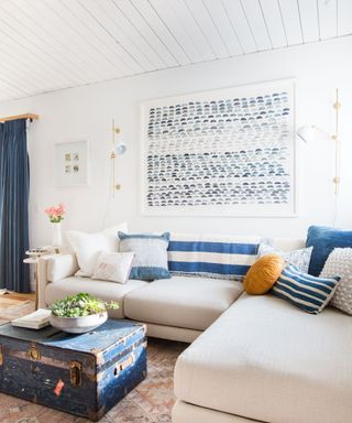 A white and blue living room with a large piece of art and two symmetrical sconces on the wall