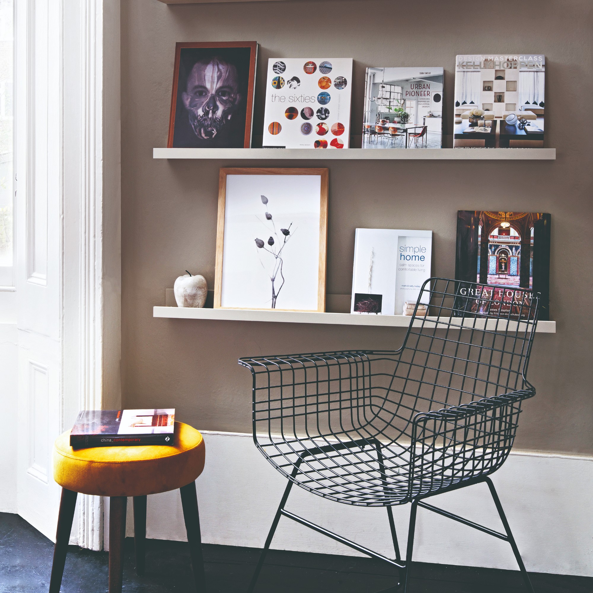 A book and print display on floating shelves with a metal wire chair in front of it