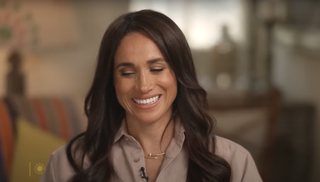 A close up of Meghan Markle on CBS wearing a blush ralph lauren shirt and matching cartier necklace