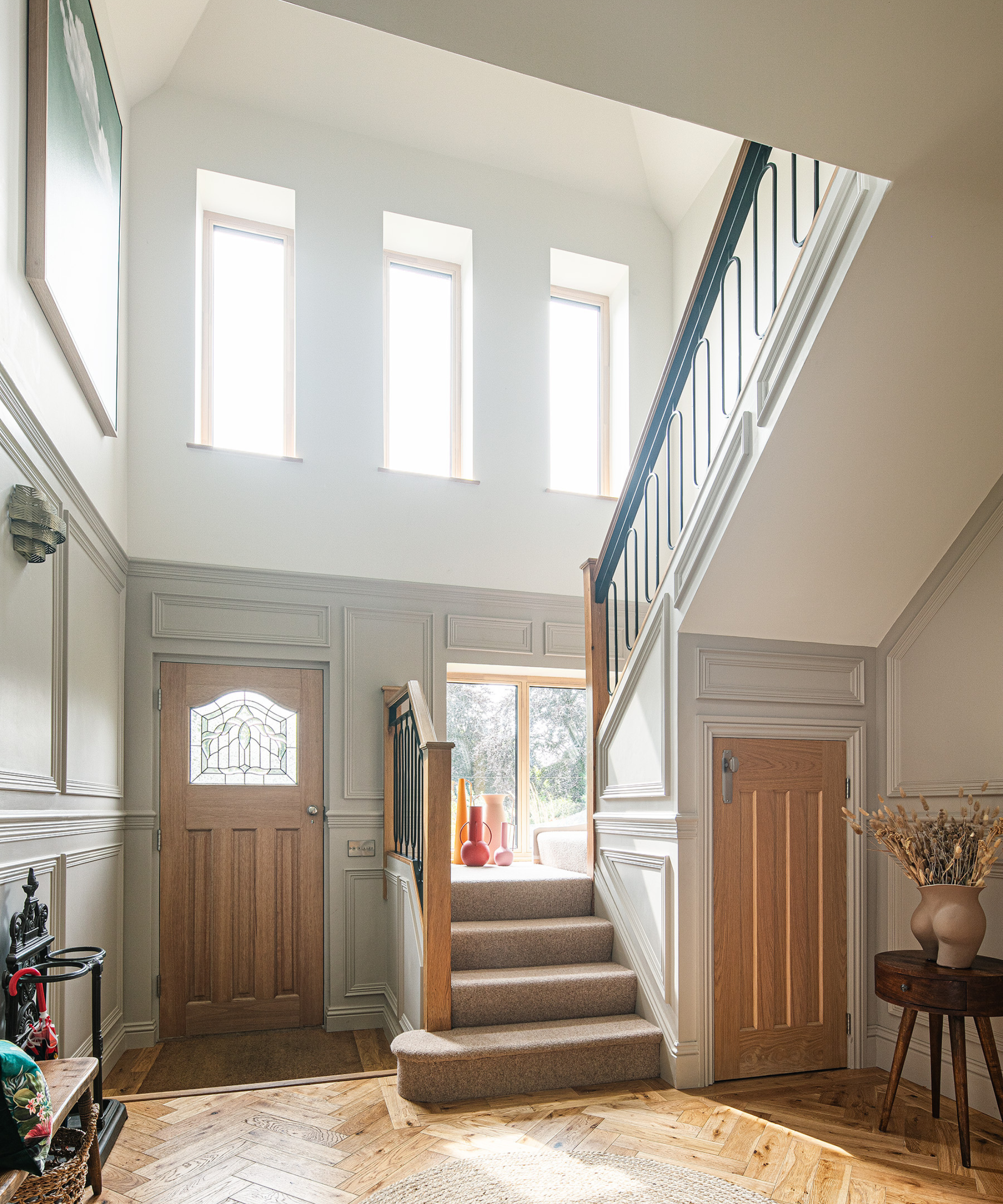 Front door entrance with wooden flooring and floors and three vertical rectangular windows above tge staircase