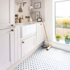 Utility room with cream cabinets and a white sink, with a blue and grey tiled floor with a broom sitting on it