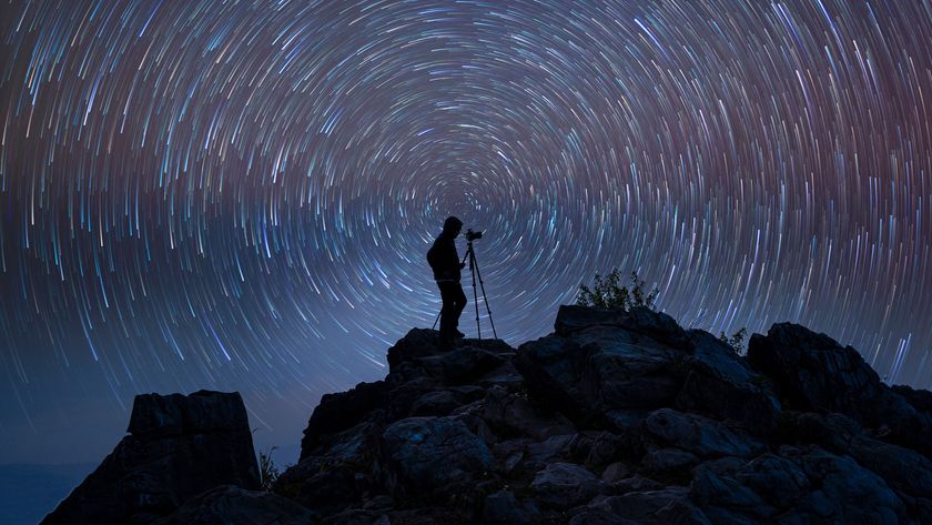 silhouette of a person using a camera on a tripod against a star trail background