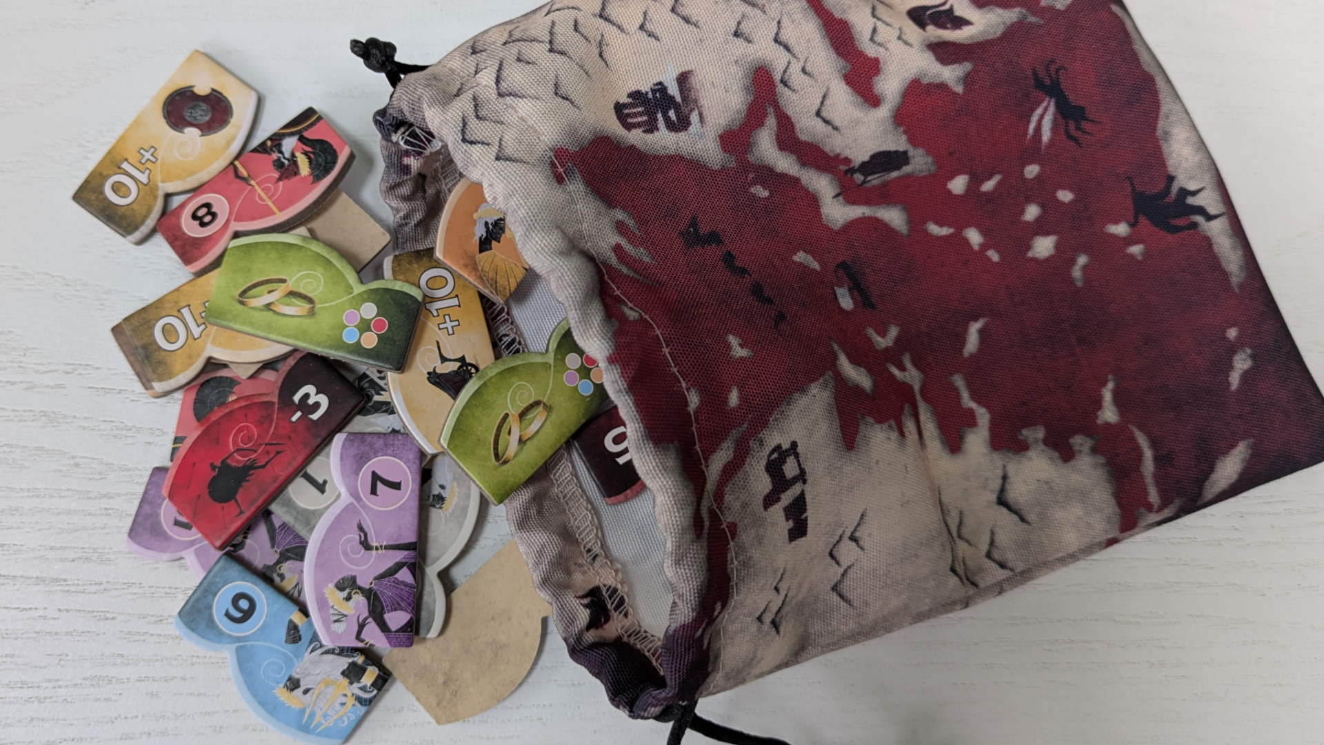 Fabric Iliad bag with tokens spilling out of it onto a white wooden surface