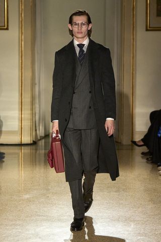 Dunhill A/W 2025 runway show featuring model on a runway wearing suit and overcoat with briefcase