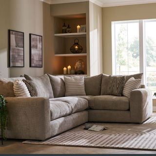 Grey corner sofa with lots of pillows against wall in living room