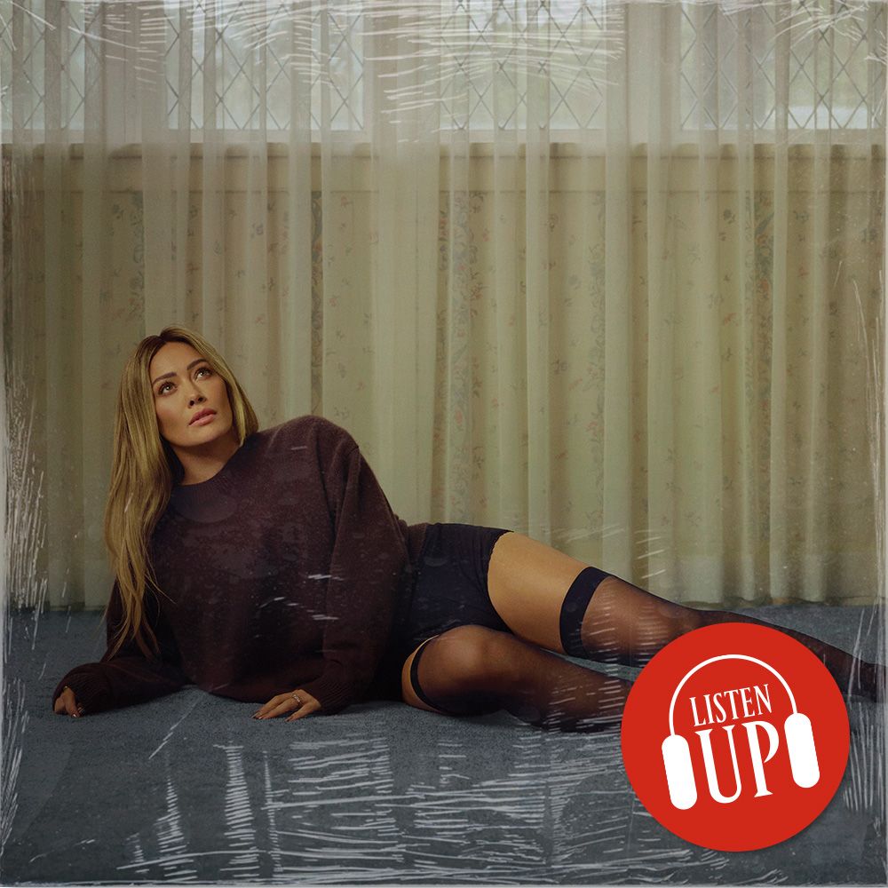 hilary duff wears a black long sleeve top as she lies on the ground in black shorts and thigh high socks on the cover of her album luck or something with the image treated with marie claire's listen up logo