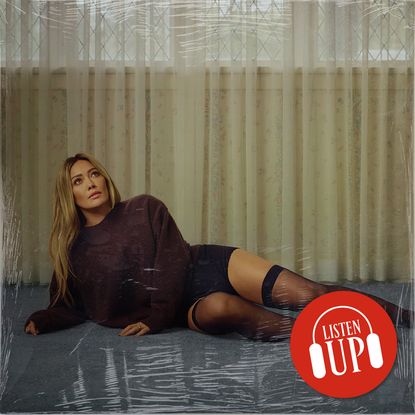 hilary duff wears a black long sleeve top as she lies on the ground in black shorts and thigh high socks on the cover of her album luck or something with the image treated with marie claire's listen up logo