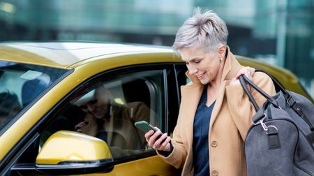 A woman with a duffel bag checks her phone before getting into her rental car.