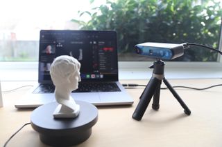 A Revopoint INSPIRE 3D Scanner on a desk, along with an object to scan and a laptop