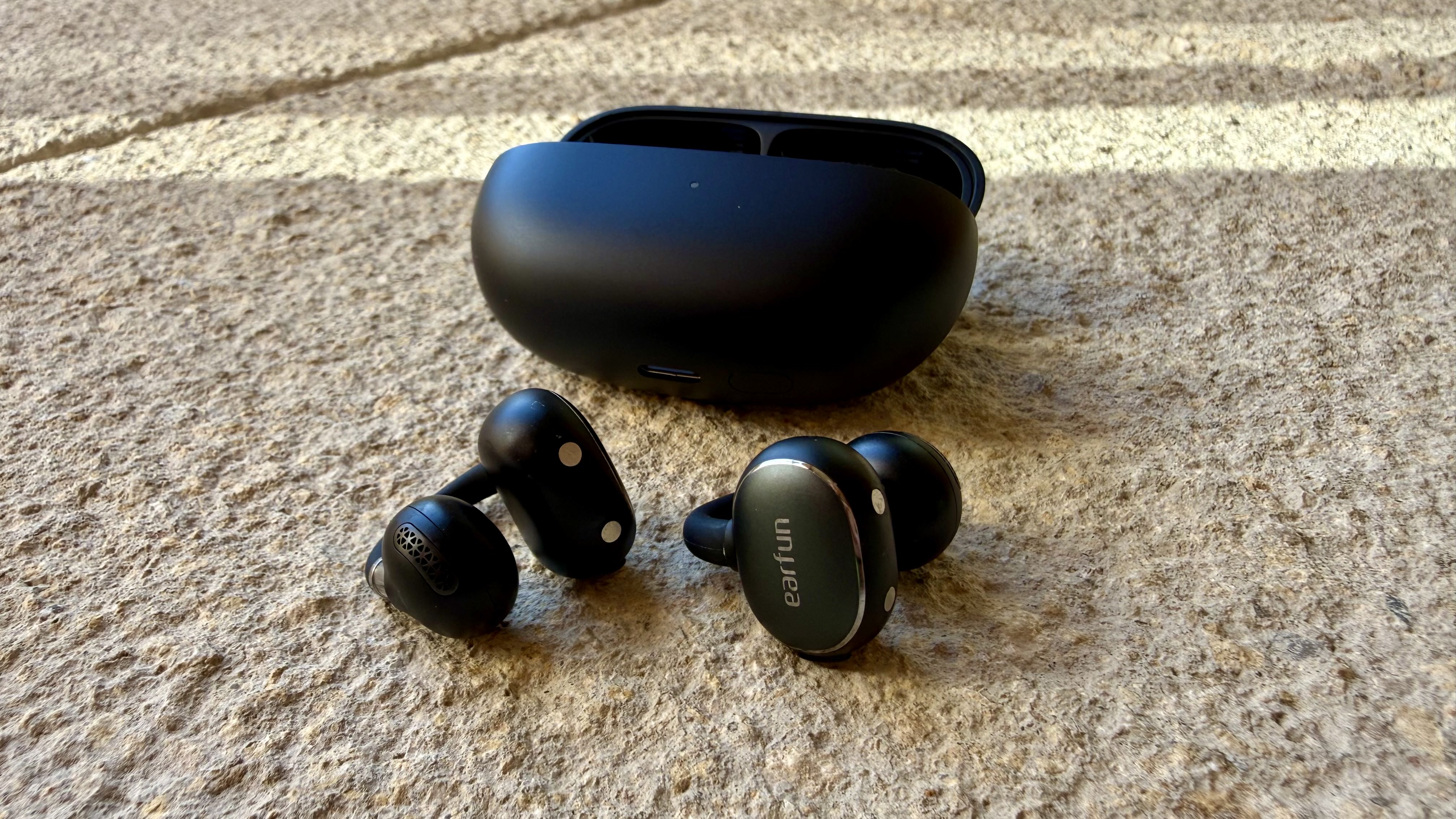 The EarFun Clip 2 earbuds on a stone surface near their charging case
