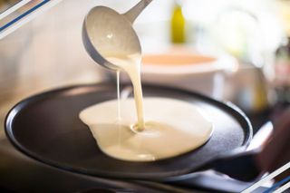 Pancake batter being poured into a frying pan with a ladel