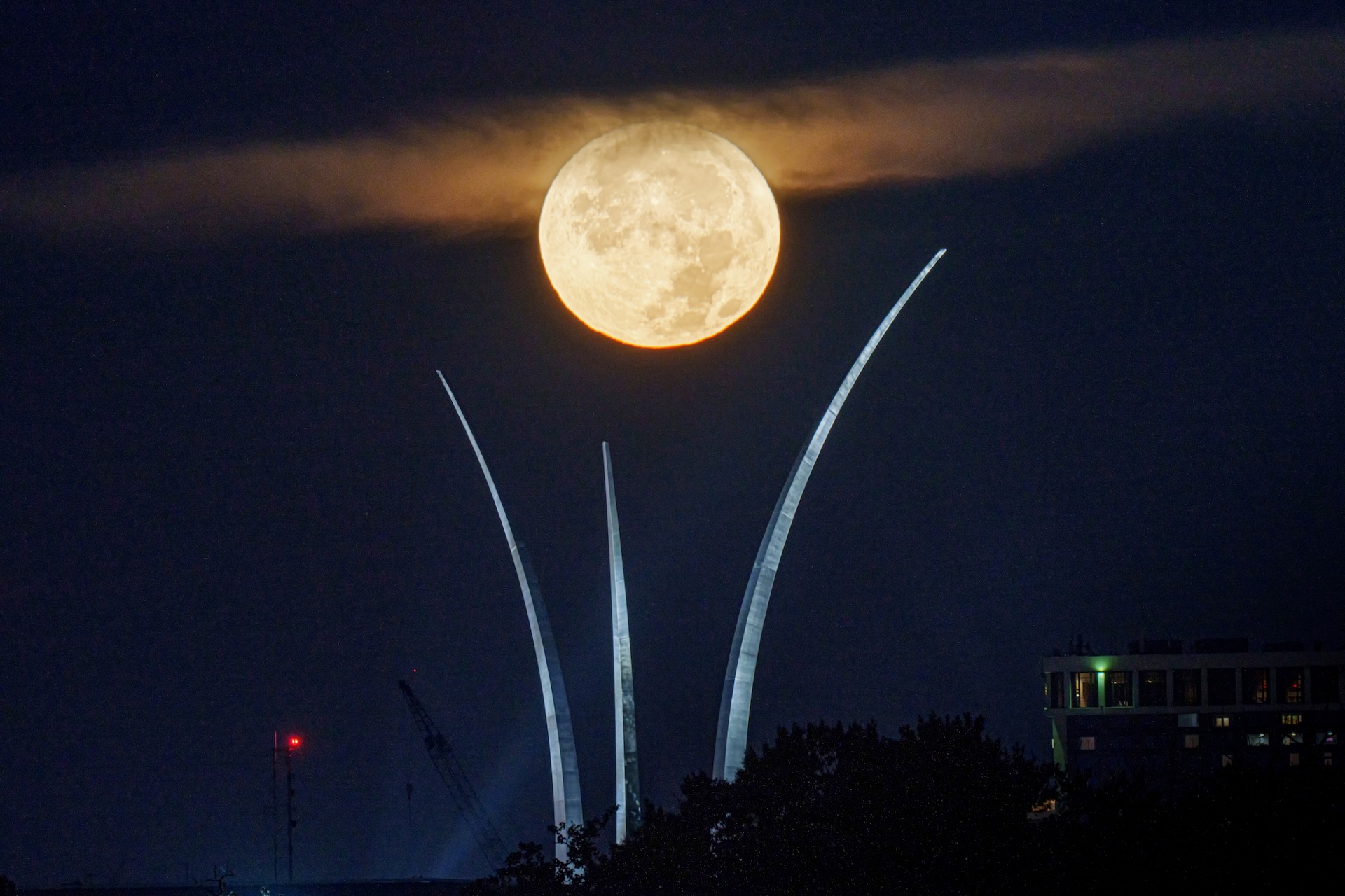 a bright full moon behind a wisp of clouds above three large towers reaching high into the sky.