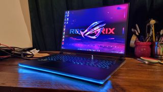 The Asus ROG Strix Scar 18 on a desk, with its RGB lights lit up in blue