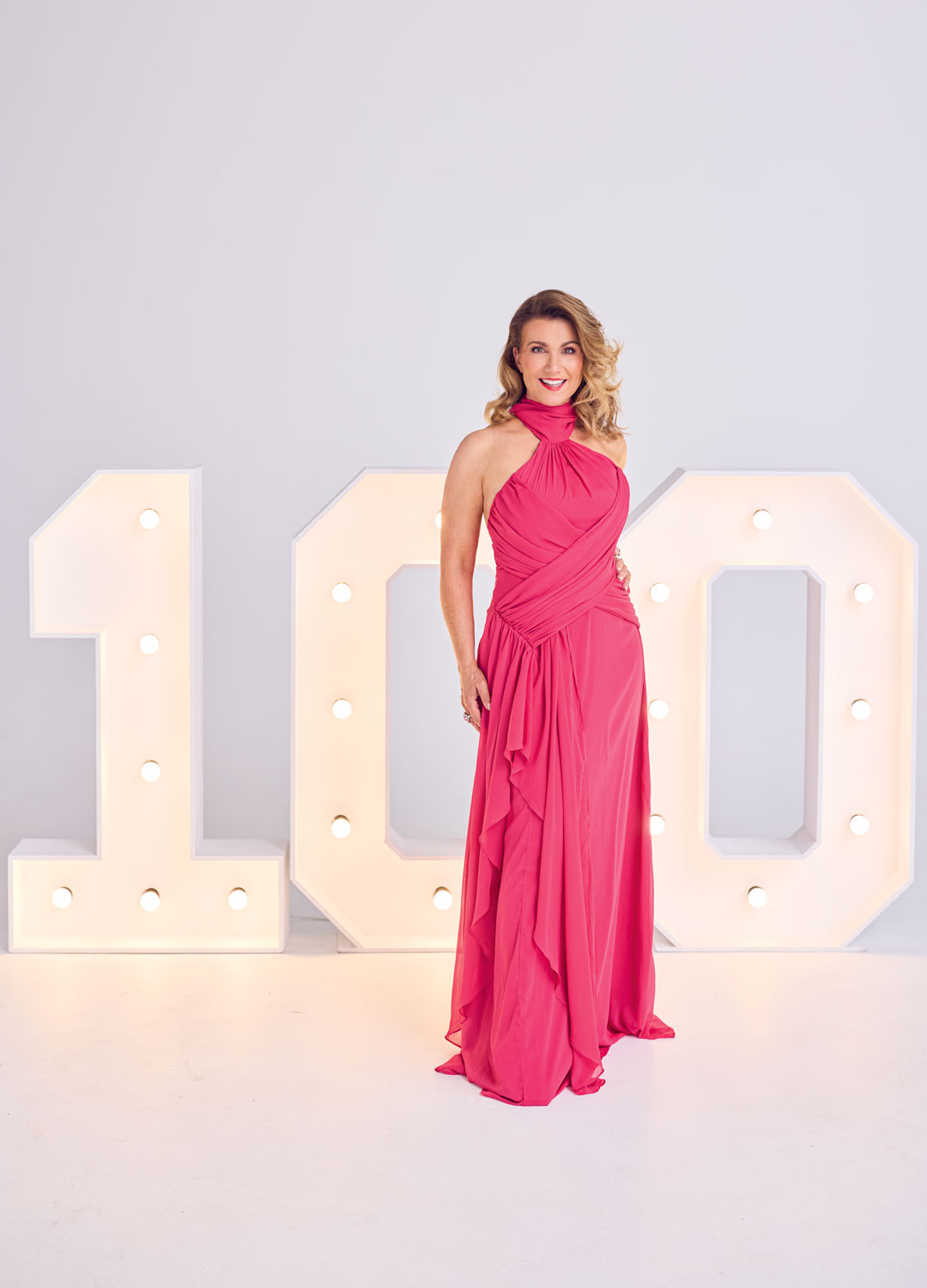 Susanna Reid in a pink halterneck dress in front of a giant 100 illumination