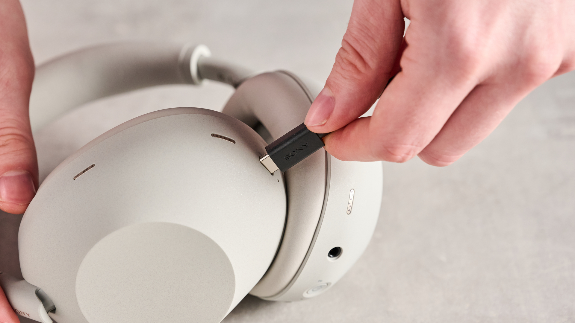Person plugging USB-C charging cable into the Sony WH-1000XM6