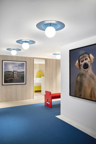 A blue carpeted hallway features a bright red bench with hanging artwork