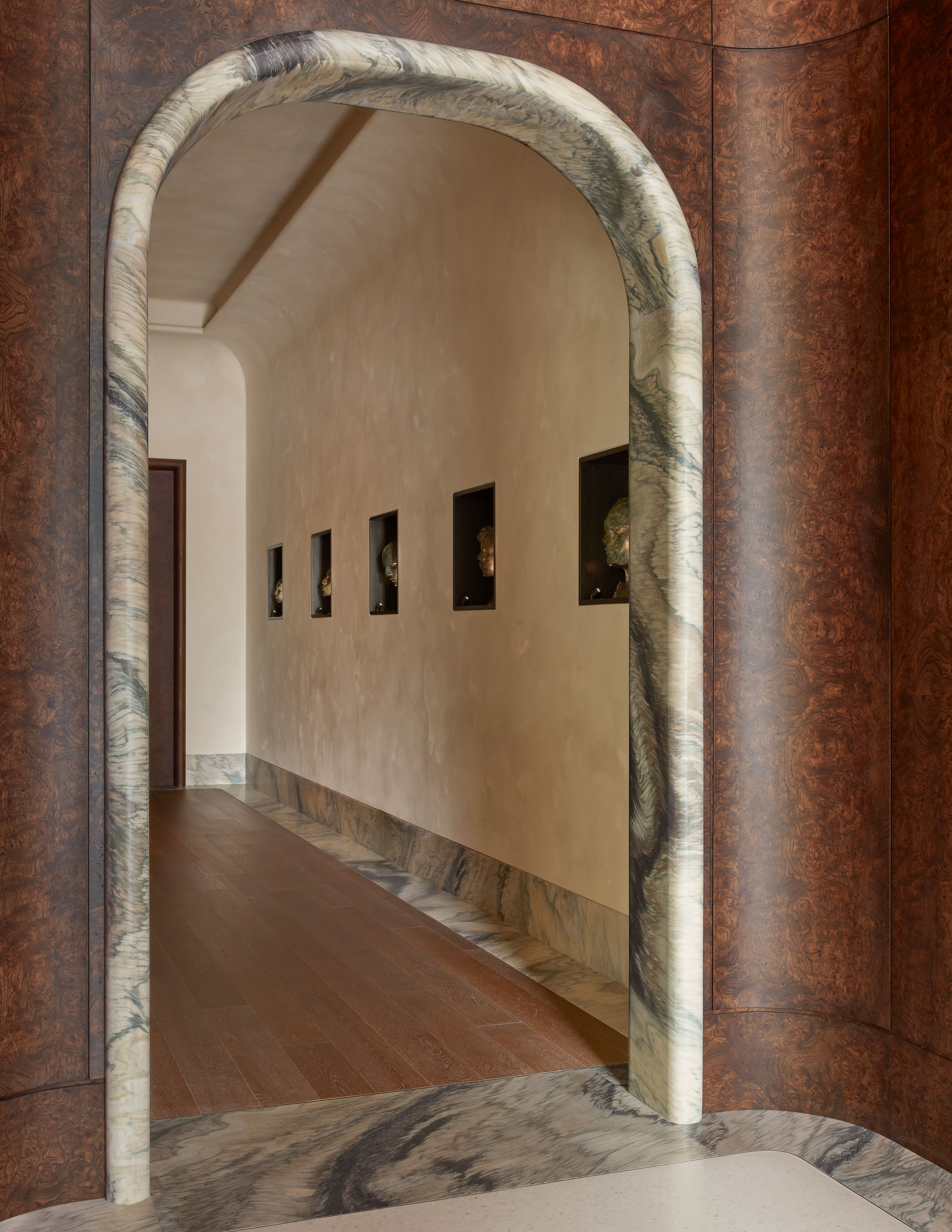 arched doorway with a marble frame into a room with wooden veneer walls and marble floors