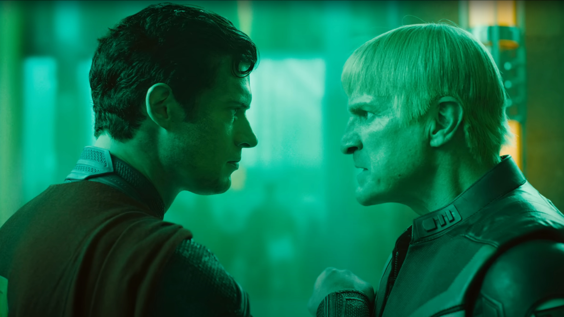 Two men, one brown haired and one with a blonde bowl cut, facing off against each other. The scene has a green hue to it.