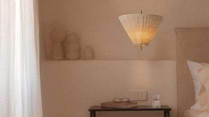 A pendant lamp with a ruched fabric shade from lights&lamps over a wood side table in a minimalist room
