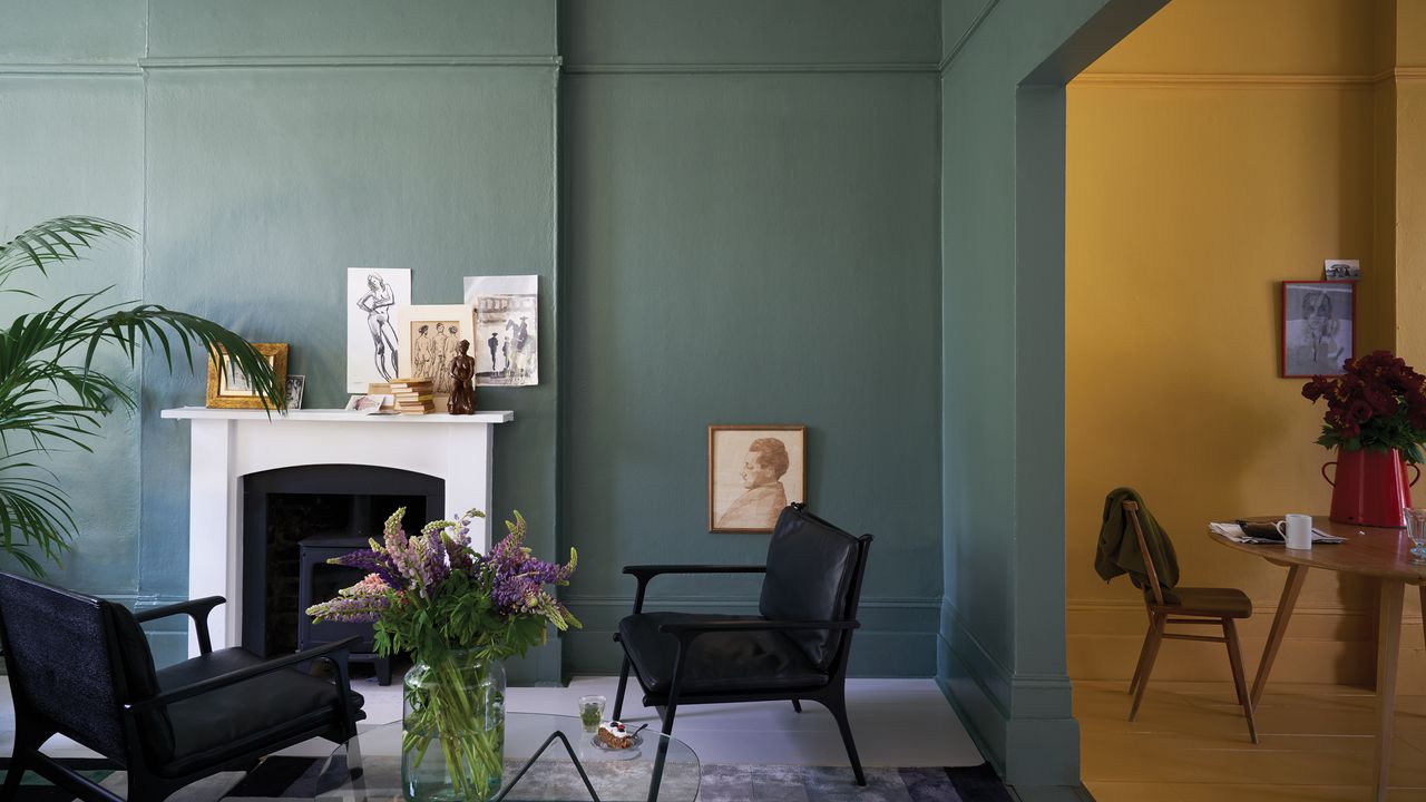 a living room using green Farrow &amp; Ball paint with a white fireplace and black furniture, and a yellow dining room to the right, some of the different paint colors for the living room to choose from