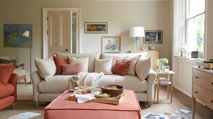 A white living room with a white couch, pink ottoman, and pink throw pillows