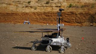 a four-wheeled rover drives in red dirt on a construction site