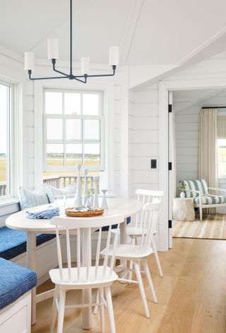 white oval dining table and chairs with blue window bench cushion in in beach house with sea view