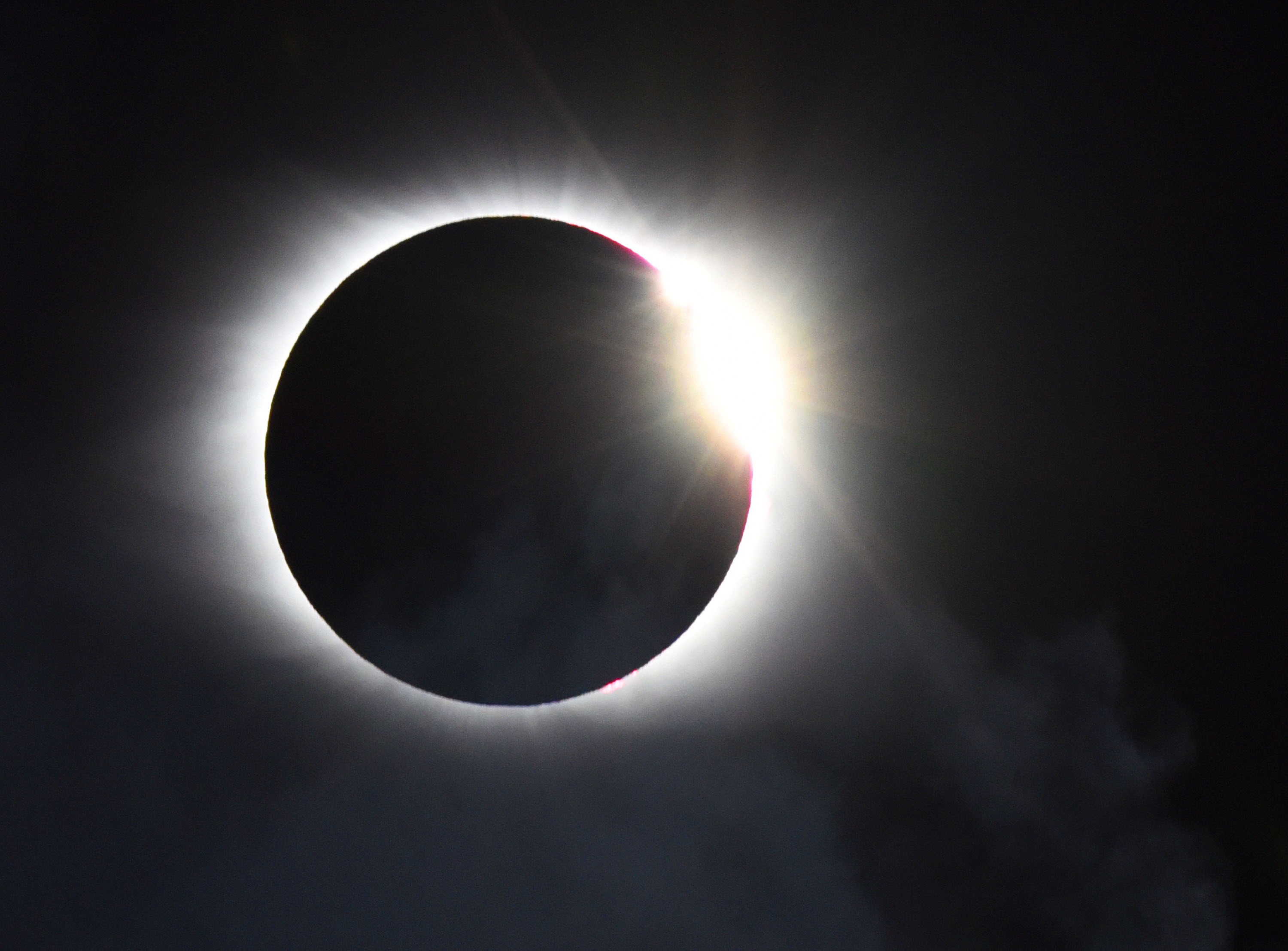 A photo of the "diamong ring" effect, captured as the last sliver of the sun's surface peeks out around the moon during a total solar eclipse in a black sky.