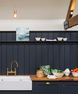 Kitchen wall paneling ideas, kitchen with dark blue tongue and groove behind white sink and along countertops, shelf, wall above painted off white