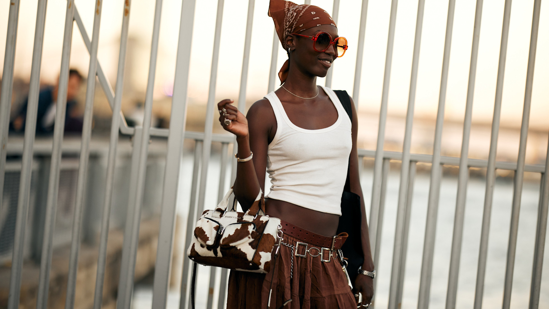 model standing in front of railings wearing a white tank and brown skirt
