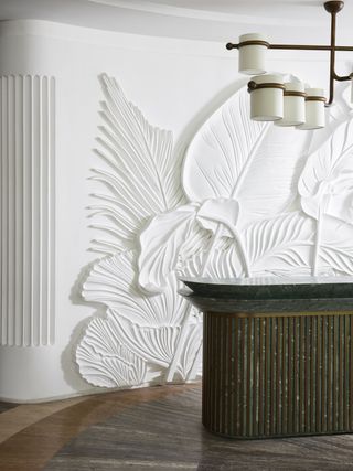 White wall with an extravagant bas relief, tropical foliage motif with a green marble island in front